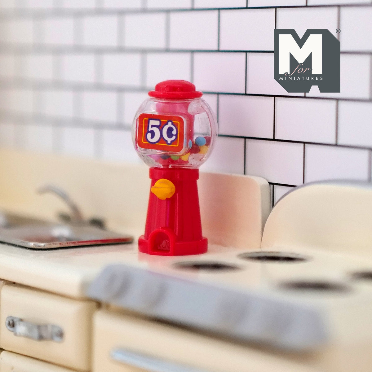 1:12 scale miniature red tabletop gumball machine with clear globe and colorful gumballs, on a kitchen counter