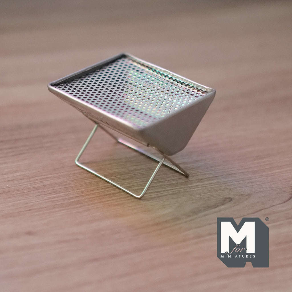 1:12 scale miniature metal charcoal grill in silver with mesh grate and folding X legs, shown on a wood surface