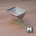 1:12 scale miniature metal charcoal grill in silver with mesh grate and folding X legs, shown on a wood surface