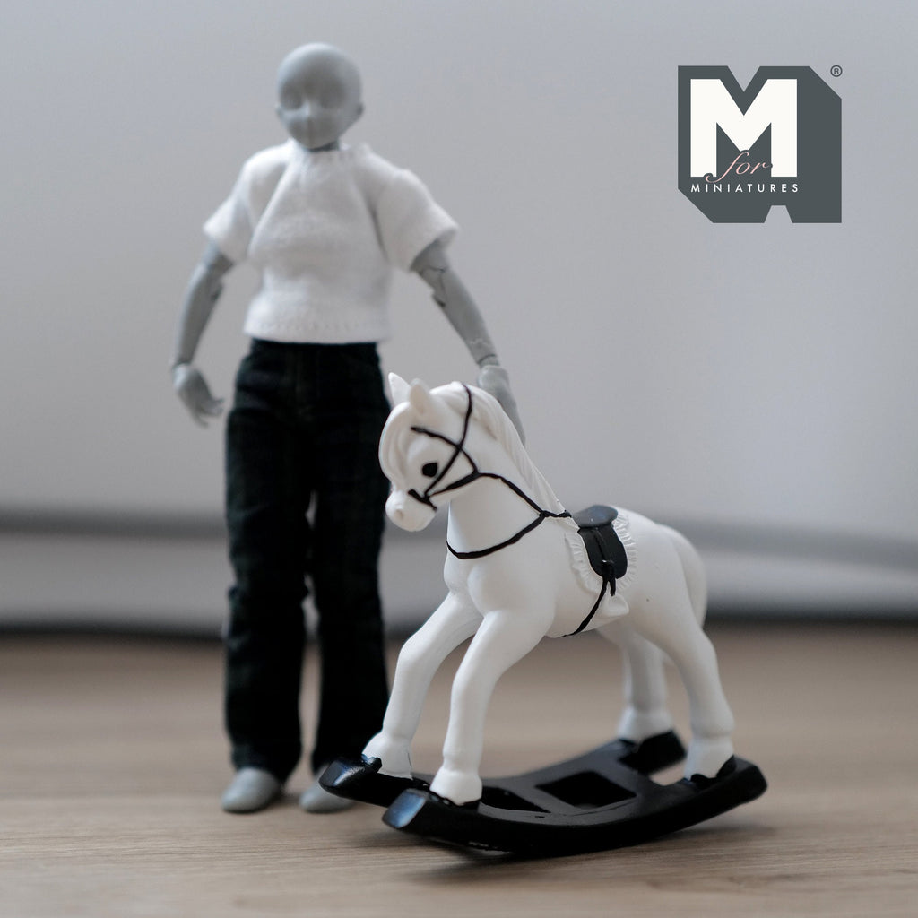 1:12 scale miniature white cast resin rocking horse with black saddle and rockers, shown beside a figure for scale