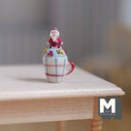 1:12 scale miniature Christmas cocoa mug in plaid with a Santa topper and red handle, shown on a wood table