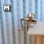 1:12 scale miniature metal meat grinder in silver with crank handle and table clamp, shown clamped to a wood table