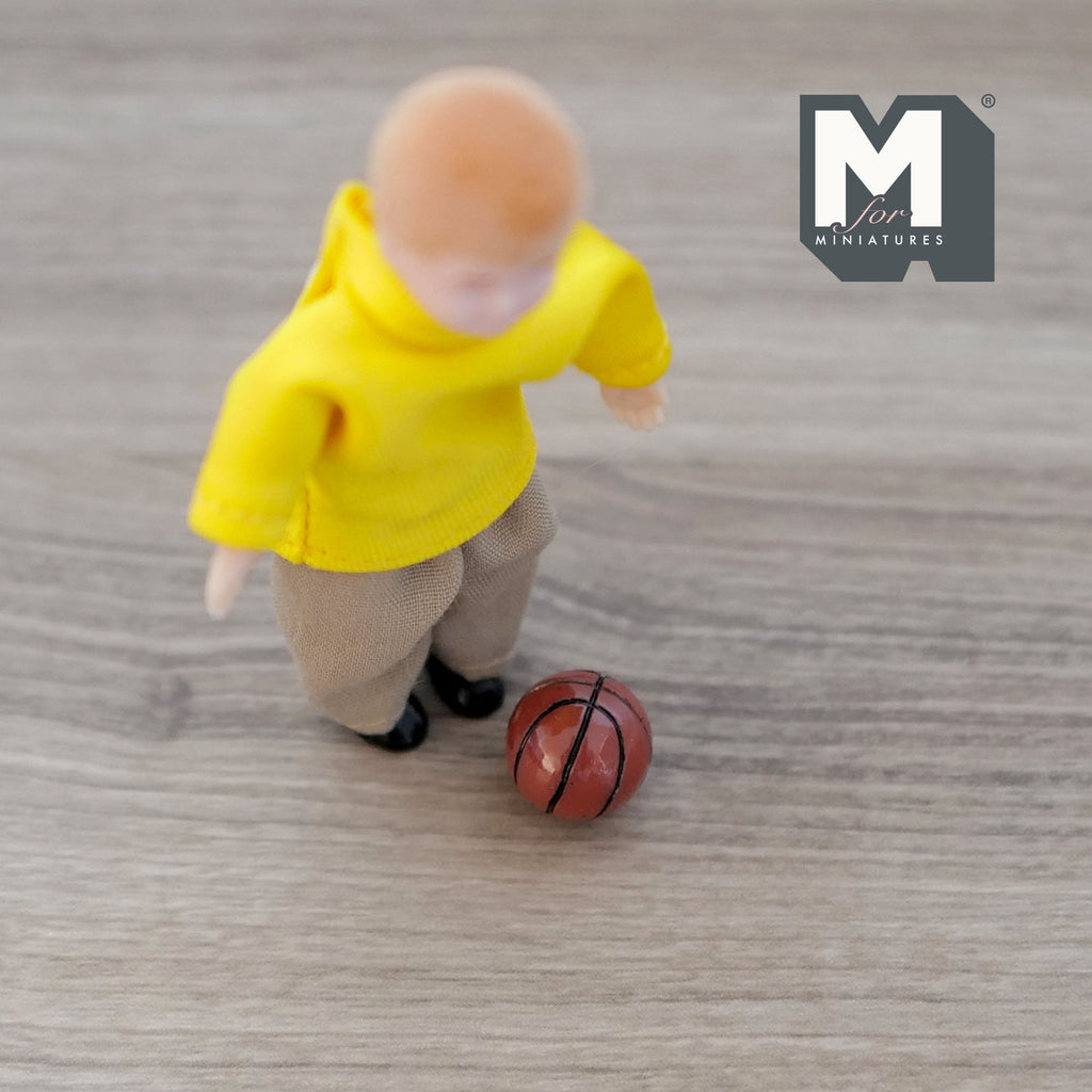 1:12 scale miniature kid's basketball in orange brown with black lines, shown on a floor beside a child figure