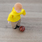 1:12 scale miniature kid's basketball in orange brown with black lines, shown on a floor beside a child figure