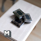 1:12 scale miniature hardcover books in black and dark gray with gold trim covers, set of 3, shown on a wood table