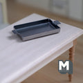 1:12 scale miniature silver metal baking tray with end handles, rectangular, shown on a white wood table