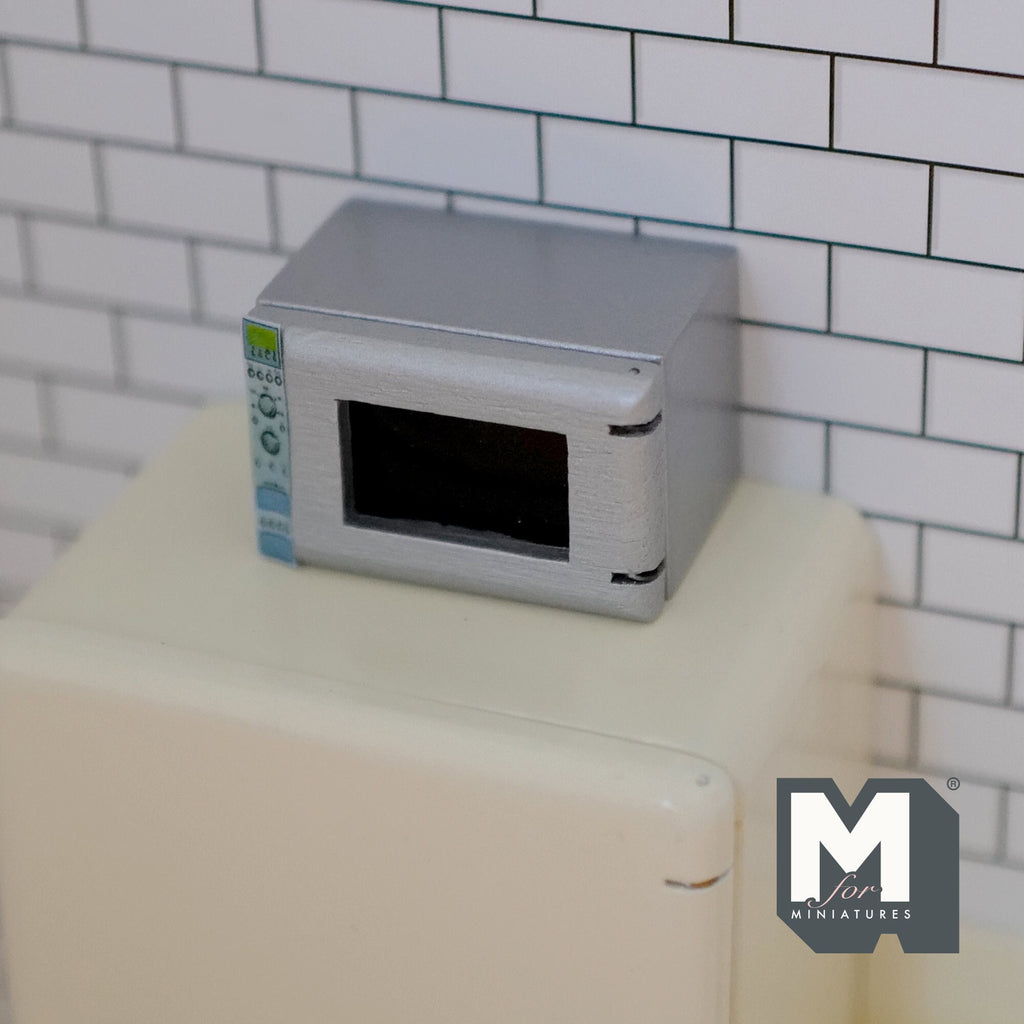 1:12 scale miniature microwave oven in silver gray with an opening door, shown on top of a cream refrigerator
