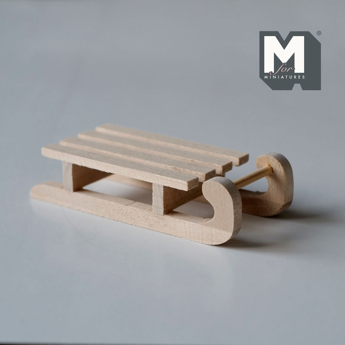 1:12 scale miniature unpainted wood slatted sledge, medium, with curved runners, shown on a gray surface