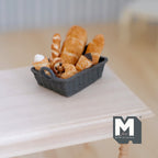 1:12 scale miniature bread basket with assorted breads, set of 8, baguettes and rolls in a gray basket on a table