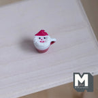 1:12 scale miniature Christmas hot drink in a Santa mug with red hat lid, white face and handle, on a pale wood table
