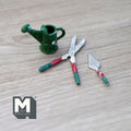 1:12 scale miniature garden tools in green and red, set of 3, watering can, trowel and shears, laid on a gray wood surface
