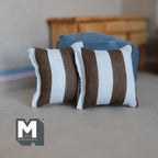 1:12 scale miniature striped square cushions in beige and brown, set of 2, wide vertical stripes, shown on a gray floor