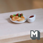 1:12 scale miniature pancake stack with strawberries and kiwi on a plate with a white syrup jug, on a wood table