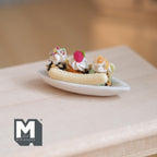 1:12 scale miniature banana split sundae in a white dish with ice cream scoops, cream and sprinkles, shown on a table