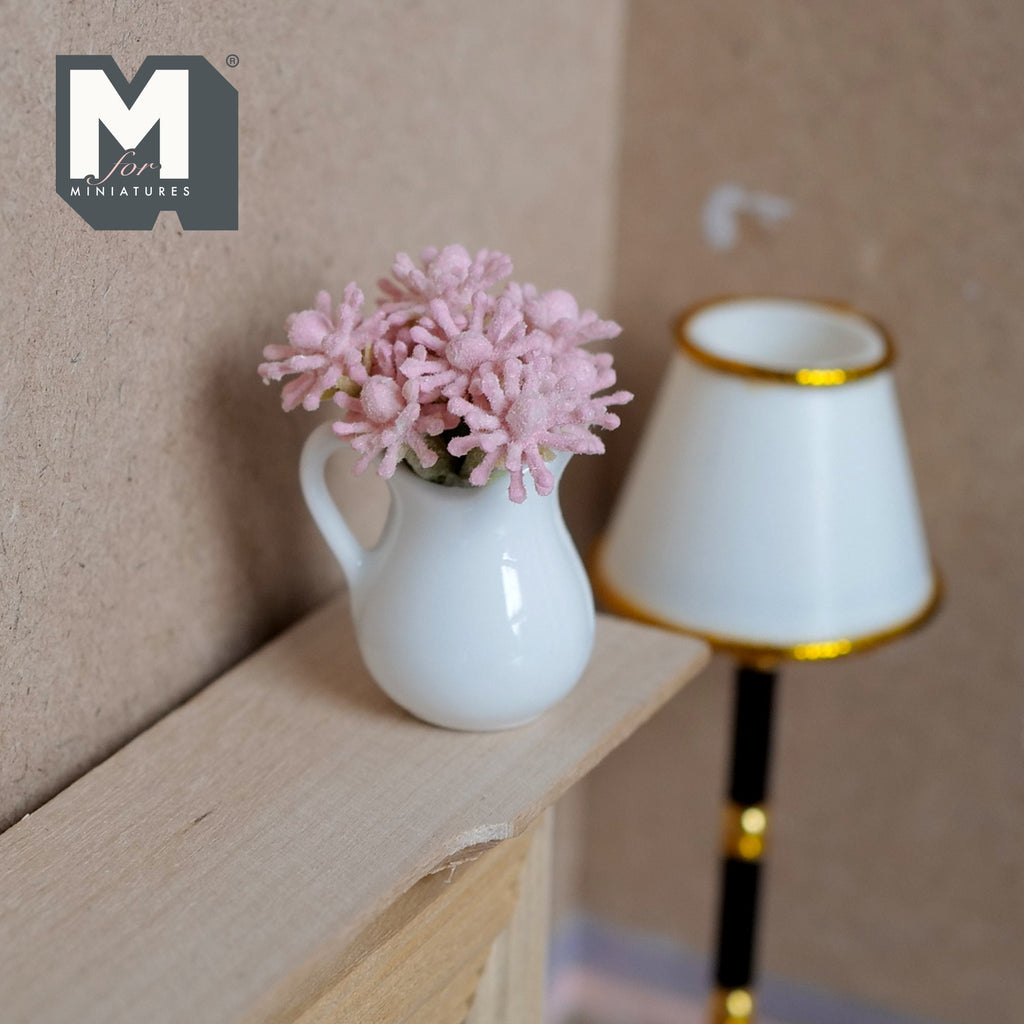 1:12 scale miniature pink flowers in a white ceramic pitcher vase, shown on a wood shelf beside a floor lamp
