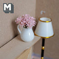 1:12 scale miniature pink flowers in a white ceramic pitcher vase, shown on a wood shelf beside a floor lamp