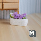 1:12 scale miniature white and lilac flowers in a long white planter trough with embossed pattern, shown on a wood floor