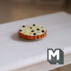 1:12 scale miniature clay banana blueberry cream pie on a metal plate, shown on a bare wood table