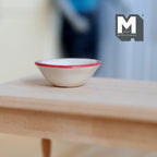 1:12 scale miniature ceramic bowl in white with a red rim, shown on a light wood table
