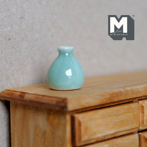 1:12 scale miniature ceramic squat bottle vase in glossy celadon green, shown on a wood dresser