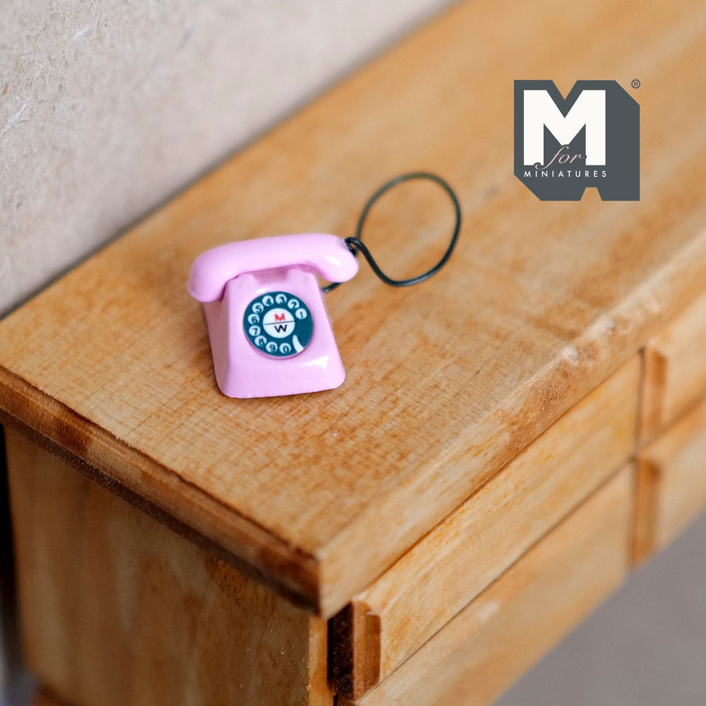 1:12 scale miniature metal rotary dial telephone in pink with blue dial and black cord, shown on a wood dresser