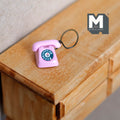 1:12 scale miniature metal rotary dial telephone in pink with blue dial and black cord, shown on a wood dresser