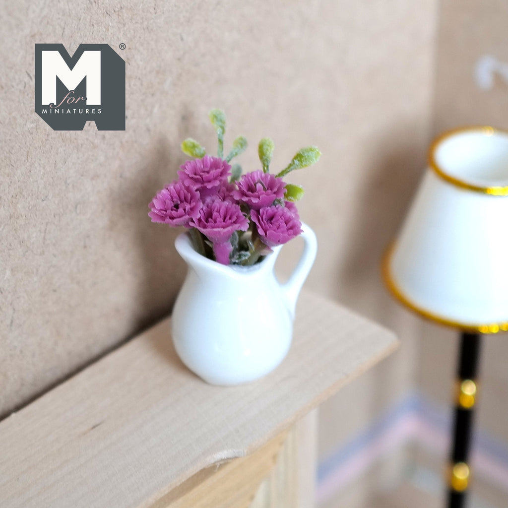 1:12 scale miniature pink carnations in a white ceramic pitcher vase, shown on a wood mantel beside a lamp