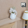 1:12 scale miniature white flowers in white ceramic jug vase, shown on a wood mantel beside a lamp