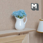 1:12 scale miniature blue flowers in a white ceramic pitcher vase, shown on a wood mantel beside a lamp