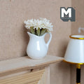 1:12 scale miniature white flowers in a white ceramic pitcher vase, shown on a wood mantel beside a lamp