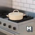 1:12 scale miniature metal cooking pot with lid in beige, round casserole style with side handles, shown on a kitchen stove