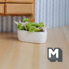 1:12 scale miniature flowers in a long white planter trough with green leaves, shown on a wood floor