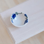 1:12 scale miniature ceramic bowl in white with dark blue floral rim, shown on a light wood tabletop