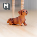 1:12 scale miniature sitting dachshund dog in brown cast resin, shown on a wood floor beside a table leg