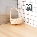 1:12 scale miniature rope basket with tall arched handle in beige, round woven style, shown on a wood counter by white tile