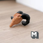 1:12 scale miniature cast resin ram skull in brown with black curled horns, shown lying on a light wood surface