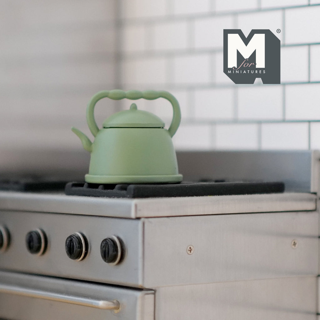 1:12 scale miniature metal kettle with lid in sage green, curved top handle and spout, shown on a kitchen stove