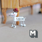1:12 scale miniature Calaveras dog figurine in white with black skeleton stripes and a red hat, on a floor