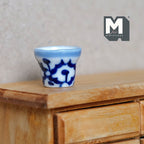 1:12 scale miniature ceramic round flower pot with blue and white pattern, shown on a wood dresser