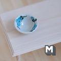1:12 scale miniature ceramic bowl in white with blue floral pattern, shown on a light wood table