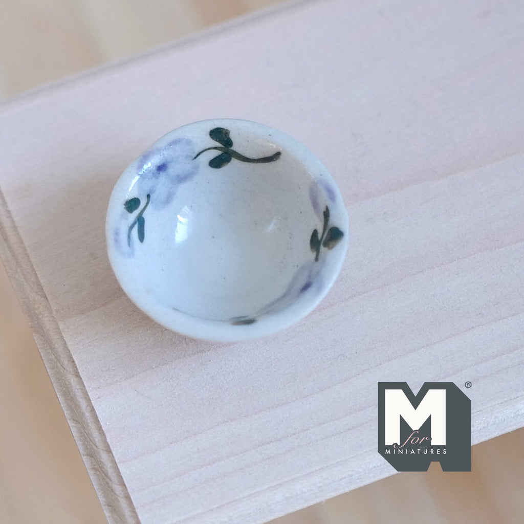 1:12 scale miniature light blue ceramic bowl with painted leaf pattern, shown on an unpainted wood table