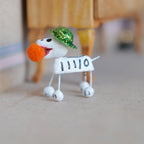 1:12 scale miniature calaveras dog figurine in white with a pom-pom nose and glittery green hat, standing on a floor