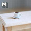 1:12 scale miniature cup of black coffee and saucer, white cup shown on a light wood table
