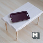 1:12 scale miniature metal baking pan in burgundy with handles, rectangular, shown on a white wood table