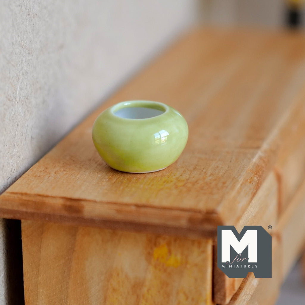 1:12 scale miniature ceramic round planter pot in light green with white interior, shown on a wood dresser