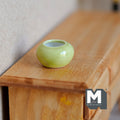 1:12 scale miniature ceramic round planter pot in light green with white interior, shown on a wood dresser