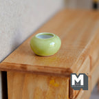 1:12 scale miniature ceramic round planter pot in light green with white interior, shown on a wood dresser
