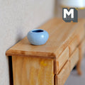 1:12 scale miniature ceramic round planter pot in light blue with glossy glaze, shown on a wood dresser
