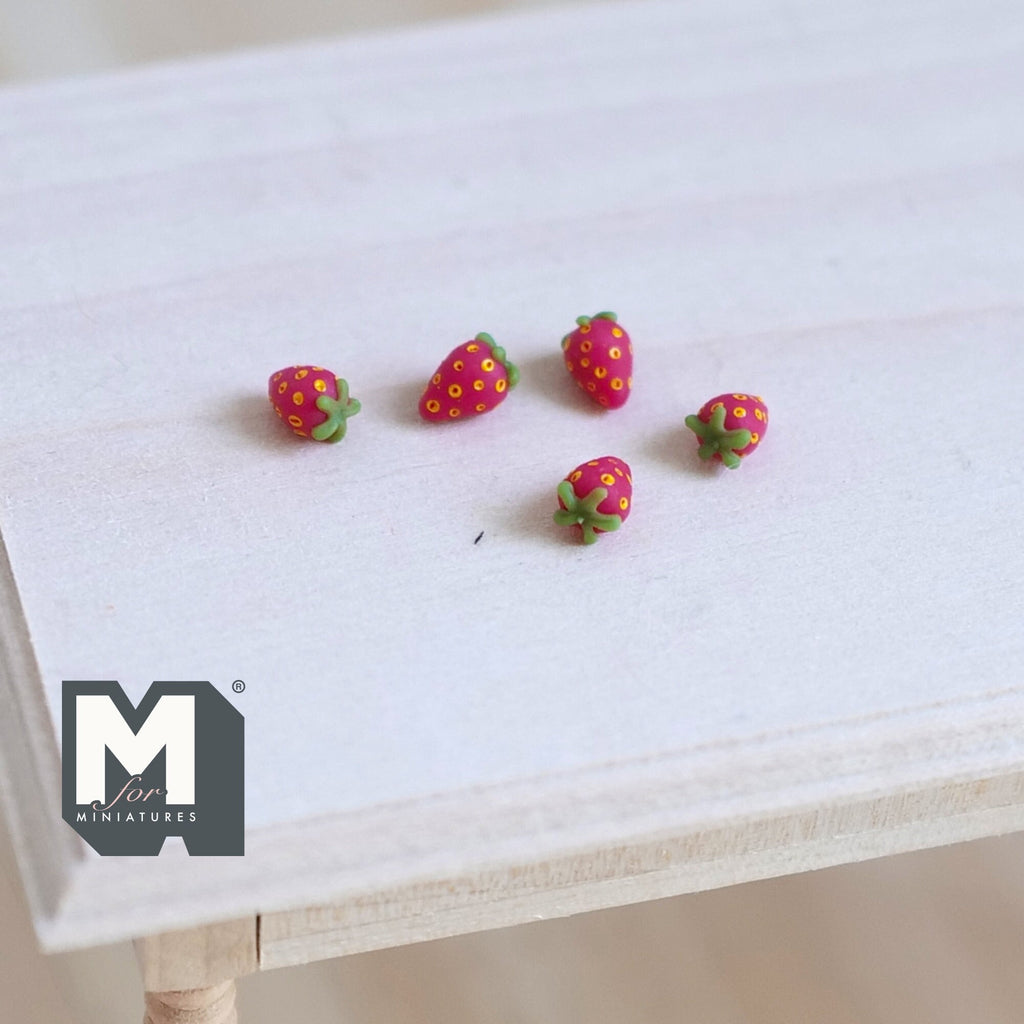 1:12 scale miniature red strawberries with green tops, set of 5, scattered on a light wood table