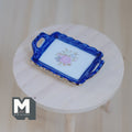 1:12 scale miniature ceramic serving tray with handles, blue rim and pink floral center, shown on a round wood table
